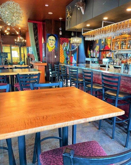 A cozy restaurant interior featuring a wooden table, black chairs, and colorful artwork on the walls.