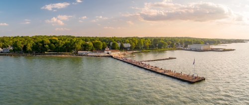 A scenic view of a pier extending into the water, surrounded by lush greenery and buildings under a sunset sky.