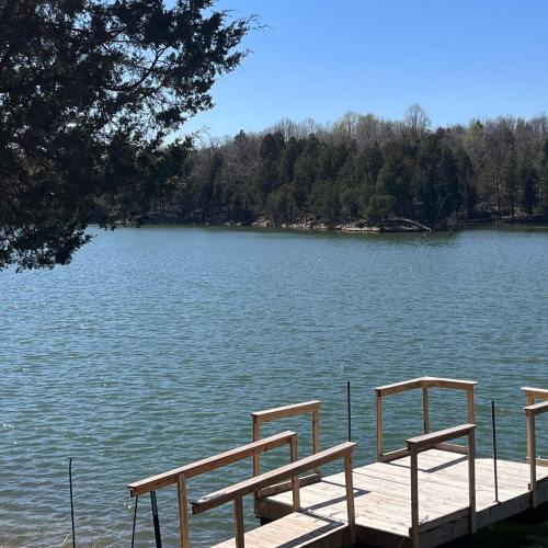 A serene lake view with a wooden dock and trees lining the shore under a clear blue sky.