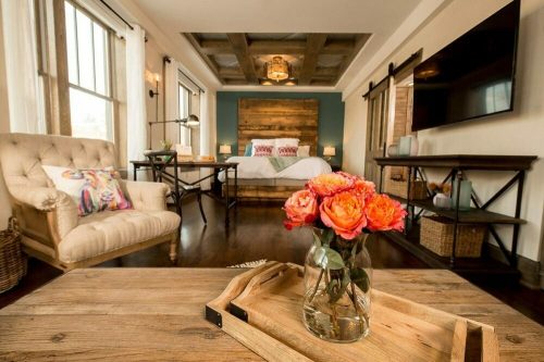 Cozy bedroom with a wooden accent wall, a plush chair, and a vase of roses on a wooden table. Warm, inviting atmosphere.