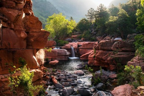 A serene landscape featuring a waterfall cascading into a rocky pool, surrounded by lush greenery and towering cliffs.
