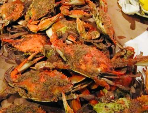 A pile of cooked crabs covered in seasoning, arranged on a brown paper surface.