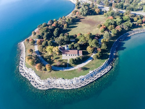 Aerial view of a small island with a park, surrounded by blue water and colorful trees in autumn.