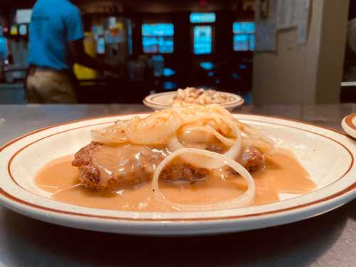 A plate of chicken fried steak topped with gravy and onions, served in a diner setting.