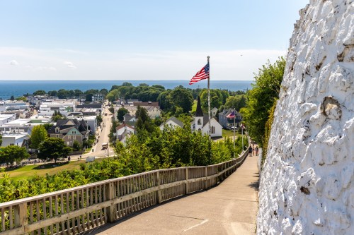 A scenic view of a pathway leading down to a coastal town, with an American flag and lush greenery in the background.