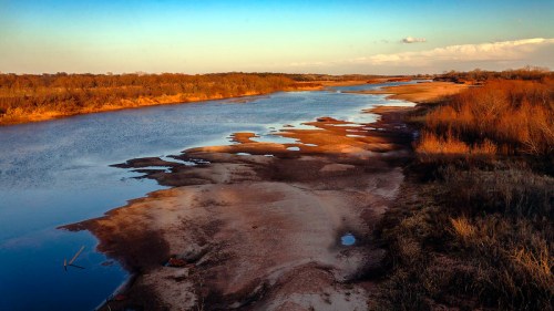 A serene river landscape at sunset, with sandy banks and gentle water reflecting the sky's colors.