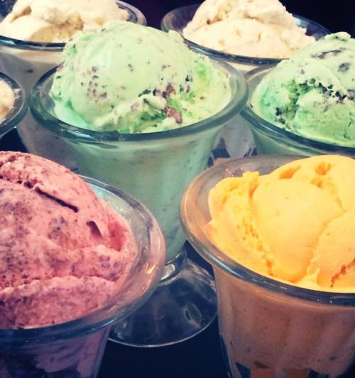 A variety of colorful ice cream scoops in glass bowls, including mint, chocolate, and yellow flavors.