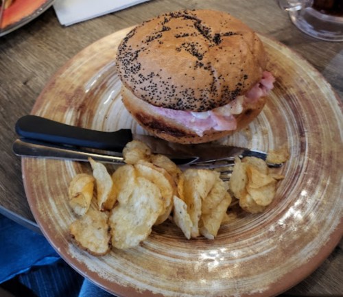 A poppy seed bun sandwich with ham and mayonnaise, served with a side of potato chips on a decorative plate.
