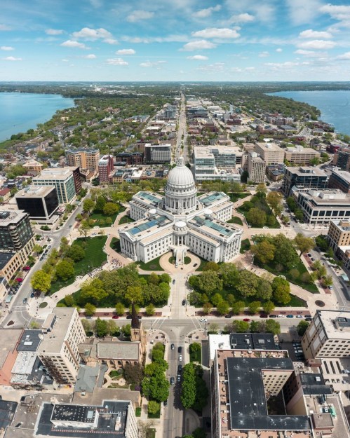 Aerial view of a city with a prominent dome building, surrounded by greenery and streets, near a large body of water.