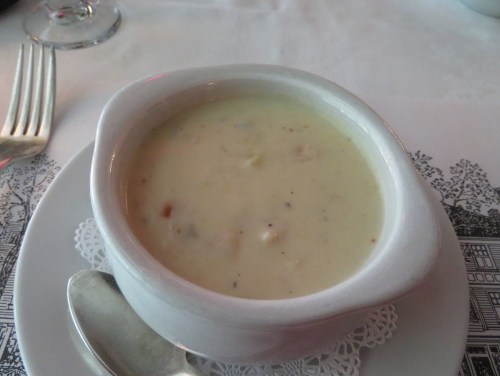 A bowl of creamy soup served in a white dish, placed on a lace doily on a table.