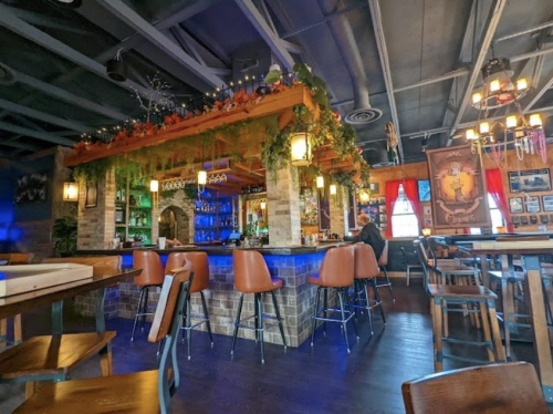 Cozy restaurant interior with a bar, wooden tables, and decorative plants, featuring warm lighting and a welcoming atmosphere.