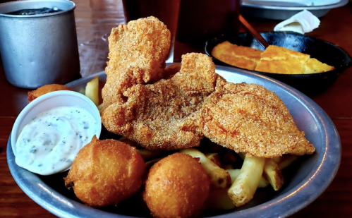 A plate of fried fish, hushpuppies, and fries, served with a side of dipping sauce.