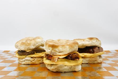 Three biscuit sandwiches with various fillings, including egg and meat, on a checkered orange and white background.