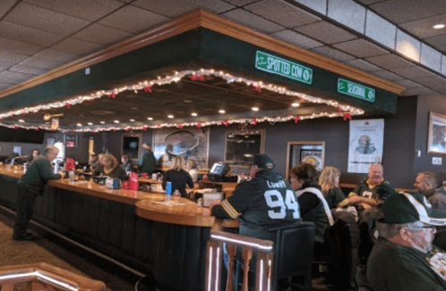 A lively bar scene with patrons wearing sports jerseys, festive decorations, and a long wooden bar.