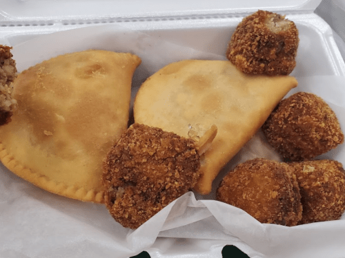 A takeout container with two golden empanadas and several crispy, round croquettes.