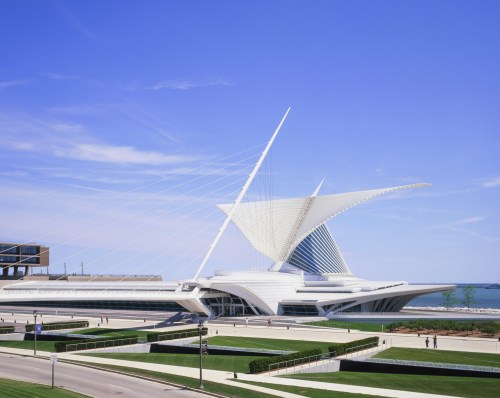 A modern architectural building with a striking sail-like design, set against a clear blue sky and green landscaping.