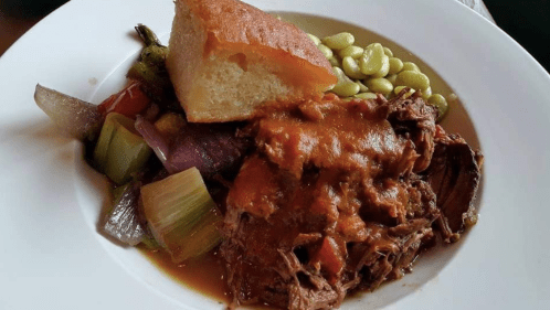 A plate of tender beef stew with vegetables, cornbread, and green beans.