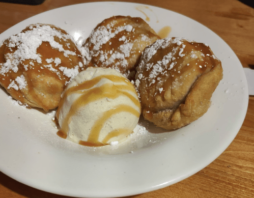 A plate with three fried dough balls drizzled with caramel and powdered sugar, alongside a scoop of vanilla ice cream.