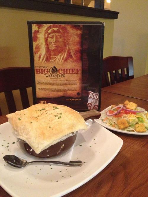 A bowl of soup topped with flaky pastry, served with a side salad and a menu featuring a Native American chief.
