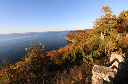 Scenic view of a river curving through autumn foliage under a clear blue sky. Stone wall in the foreground.