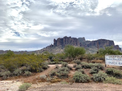 Desert landscape with rugged mountains in the background and a weathered sign for Goldfield Mine in the foreground.