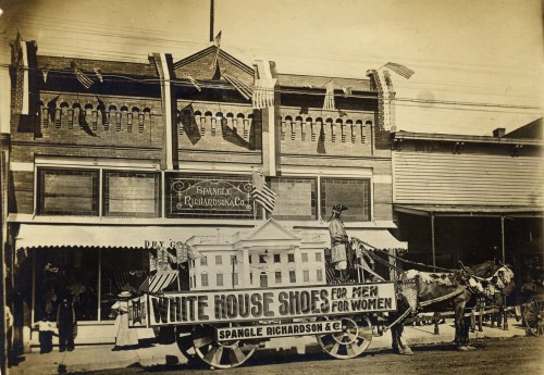 Historic photo of a horse-drawn wagon advertising "White House Shoes" in front of a storefront, with flags displayed.