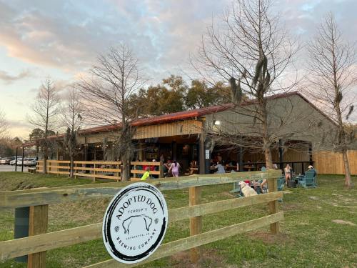 A brewery with outdoor seating, surrounded by trees, featuring a sign that reads "Adopted Dog Brewing Company."