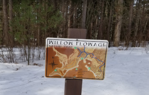 Sign for Willow Flowage Nature Trail, featuring a map and trail markers, surrounded by snow-covered trees.