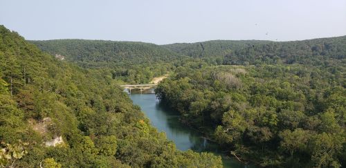 A scenic view of a river winding through lush green hills under a clear sky.