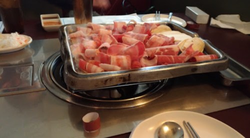 A table set for a meal with a grill, featuring strips of meat and side dishes ready for cooking.