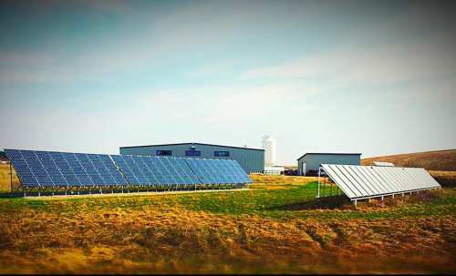 A solar panel installation beside a modern building in a grassy field under a clear sky.