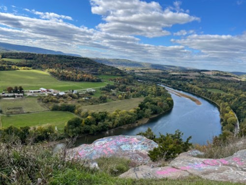 A scenic view of a winding river surrounded by lush green fields and rolling hills under a partly cloudy sky.