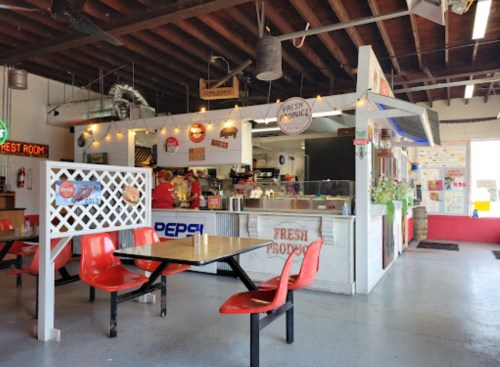 A cozy diner interior with red chairs, a counter displaying fresh produce, and vintage signs on the walls.