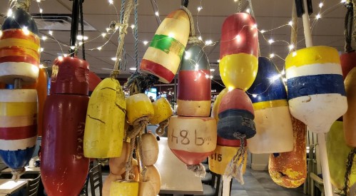 Colorful fishing buoys hanging decoratively with string lights in a cozy restaurant setting.
