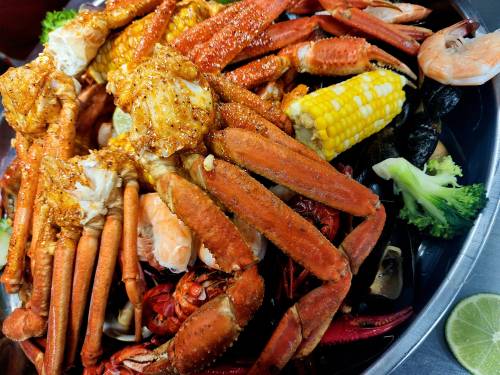 A colorful seafood platter featuring crabs, shrimp, corn, and broccoli, seasoned and arranged on a large tray.