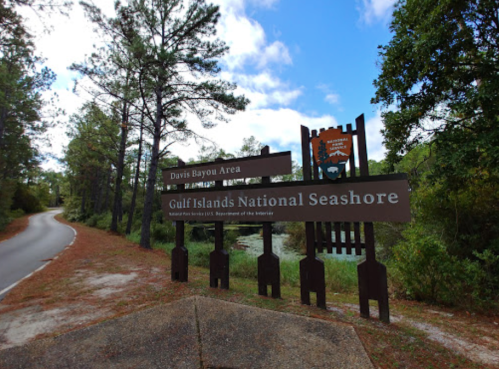 Sign for Davis Bayou Area and Gulf Islands National Seashore, surrounded by trees and a scenic pathway.
