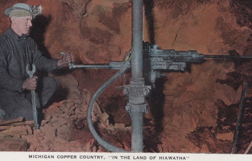 A miner operates machinery in a copper mine, wearing a headlamp and holding a wrench, in Michigan's Copper Country.