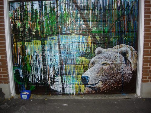 A colorful mural of a bear in a forest setting, with vibrant paint drips and a serene background of trees and water.
