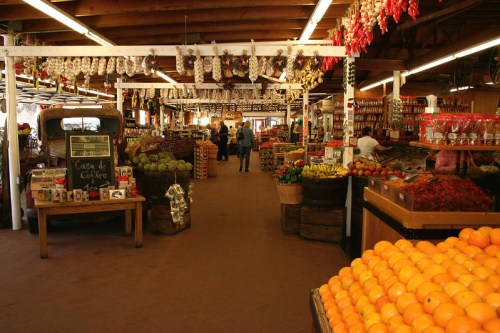A vibrant market interior filled with fresh produce, colorful displays, and shoppers browsing among the stalls.