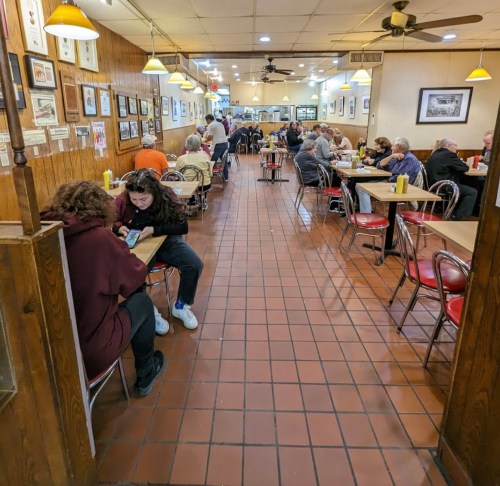 A busy diner with patrons seated at tables, chatting and enjoying meals in a cozy, casual atmosphere.