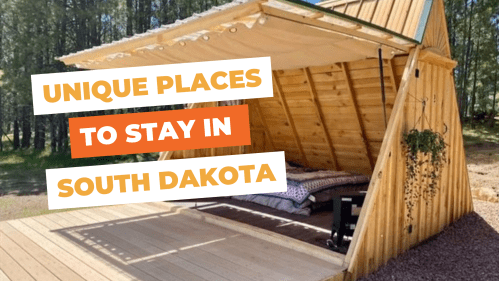 A cozy wooden A-frame structure with a bed, surrounded by trees, promoting unique stays in South Dakota.