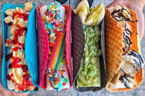 A colorful assortment of ice cream tacos filled with various toppings and flavors, held by a hand.