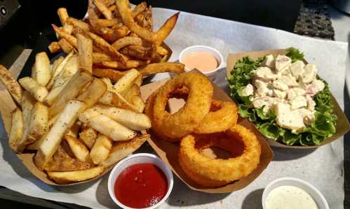 A plate of crispy fries, onion rings, and a salad with chicken, accompanied by dipping sauces.