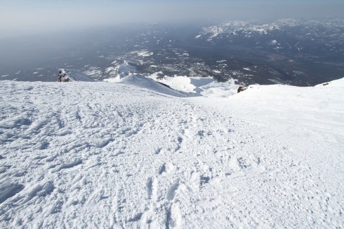 A snowy mountain landscape with a view of distant valleys and peaks under a clear sky.