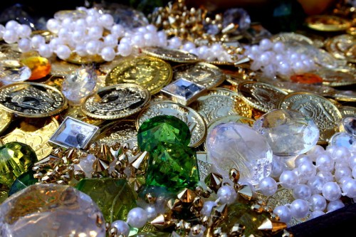 A close-up of a treasure trove featuring gold coins, colorful gemstones, and strands of pearls.