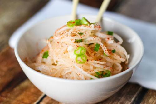 A bowl of thinly sliced white noodles topped with green onions and a sprinkle of seasoning.