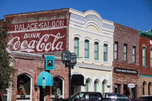 Historic buildings with a faded Coca-Cola mural, featuring brick facades and a clear blue sky.