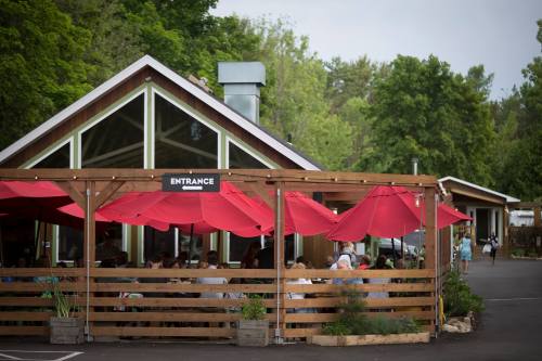A restaurant with a wooden exterior and red umbrellas, featuring a sign that says "Entrance" and surrounded by greenery.