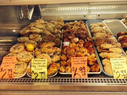 A display case filled with various seafood dishes, including stuffed clams and shrimp, with price tags visible.