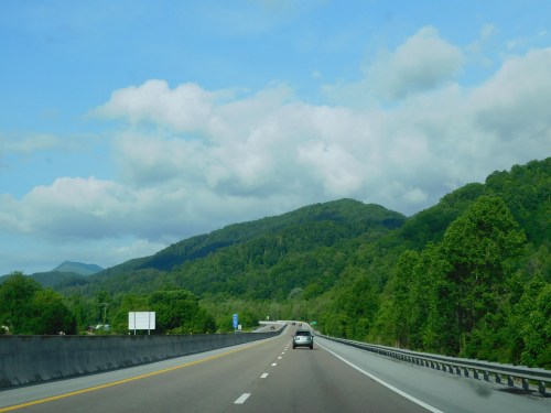 A scenic highway stretches through lush green mountains under a partly cloudy sky.